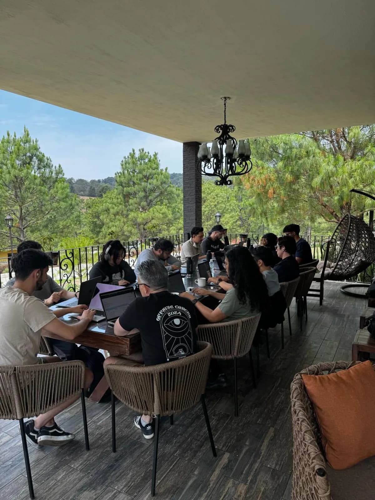The Keep team working on laptops around a long table on an open terrace surrounded by pine trees